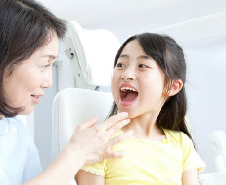 口を開いて、女性の歯科衛生士に口の中を見せている女の子。